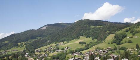 A village nestled in a valley with houses and buildings spread across the landscape, surrounded by green hills and a clear sky.