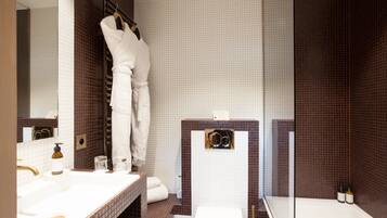 Un baño moderno con un lavamanos blanco, cabina de ducha con mampara de vidrio y un espejo grande.