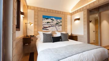 A hotel room with a large bed, a painting of a snowy landscape, a nightstand with a lamp, and a wooden floor.