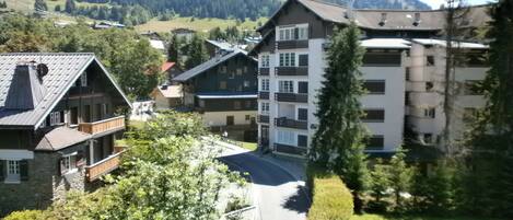 A mountain resort with traditional chalet-style buildings, a paved road, and a forested backdrop.