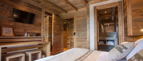 Ein Interieur einer Holzhütte mit einem Bett, einem an der Wand befestigten Fernseher und einem Holztisch mit Stuhl.