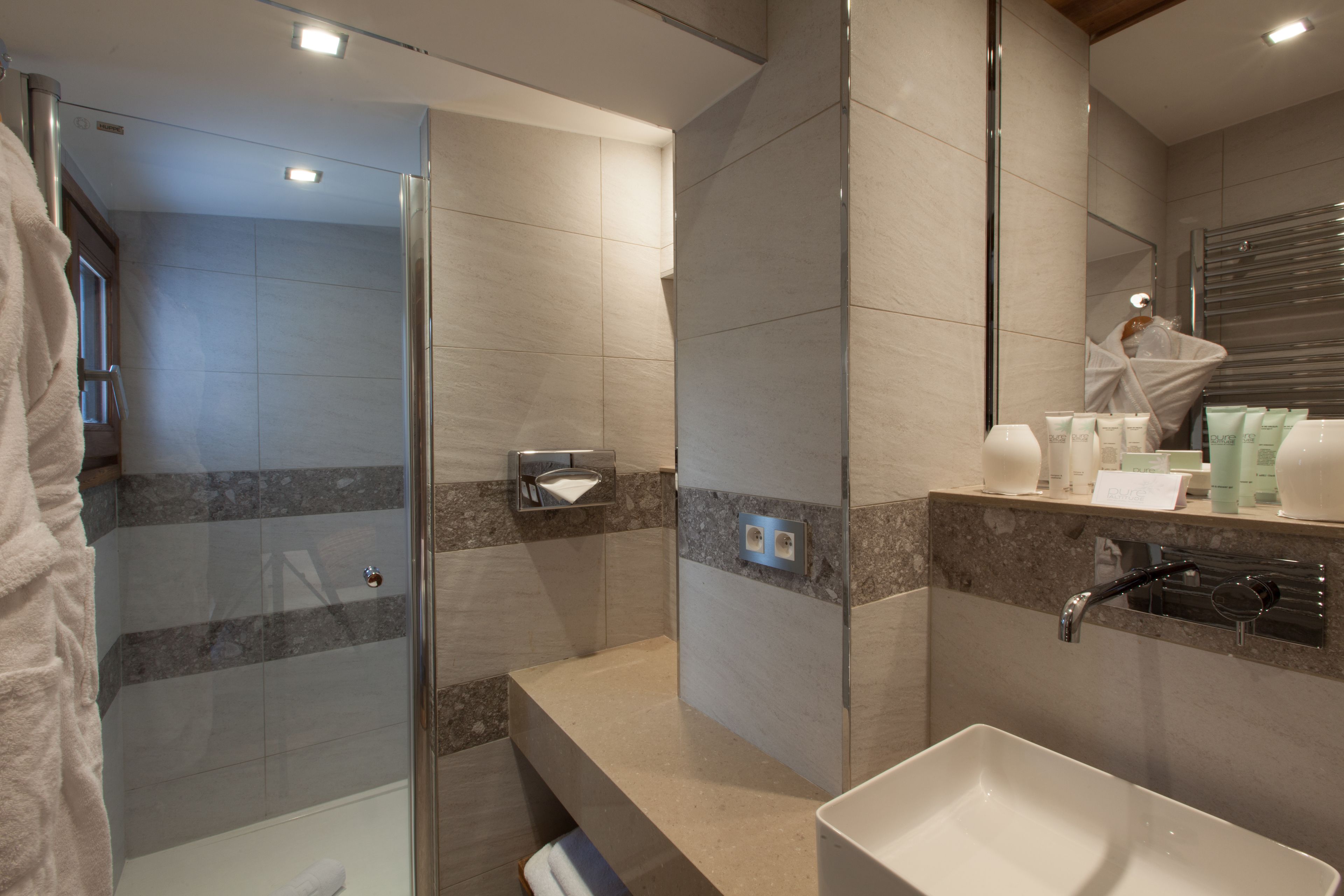 A modern bathroom with a glass shower enclosure, a large sink, and a vanity with toiletries.