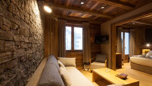 Una habitación acogedora con pared de piedra, techo de madera, un sofá, una mesa de centro de madera y una cama.