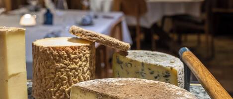 A cheese selection on a marble counter in a rustic room with wooden walls and tables set for dining.