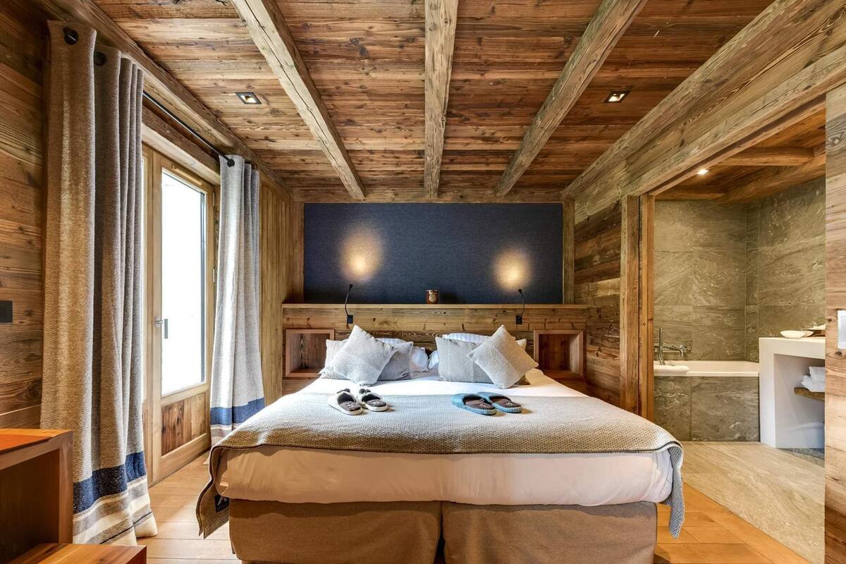 Ein Schlafzimmer in einer Holzhütte mit einem großen Bett, einem Flachbildfernseher und einem Badezimmer mit Waschbecken und Spiegel.