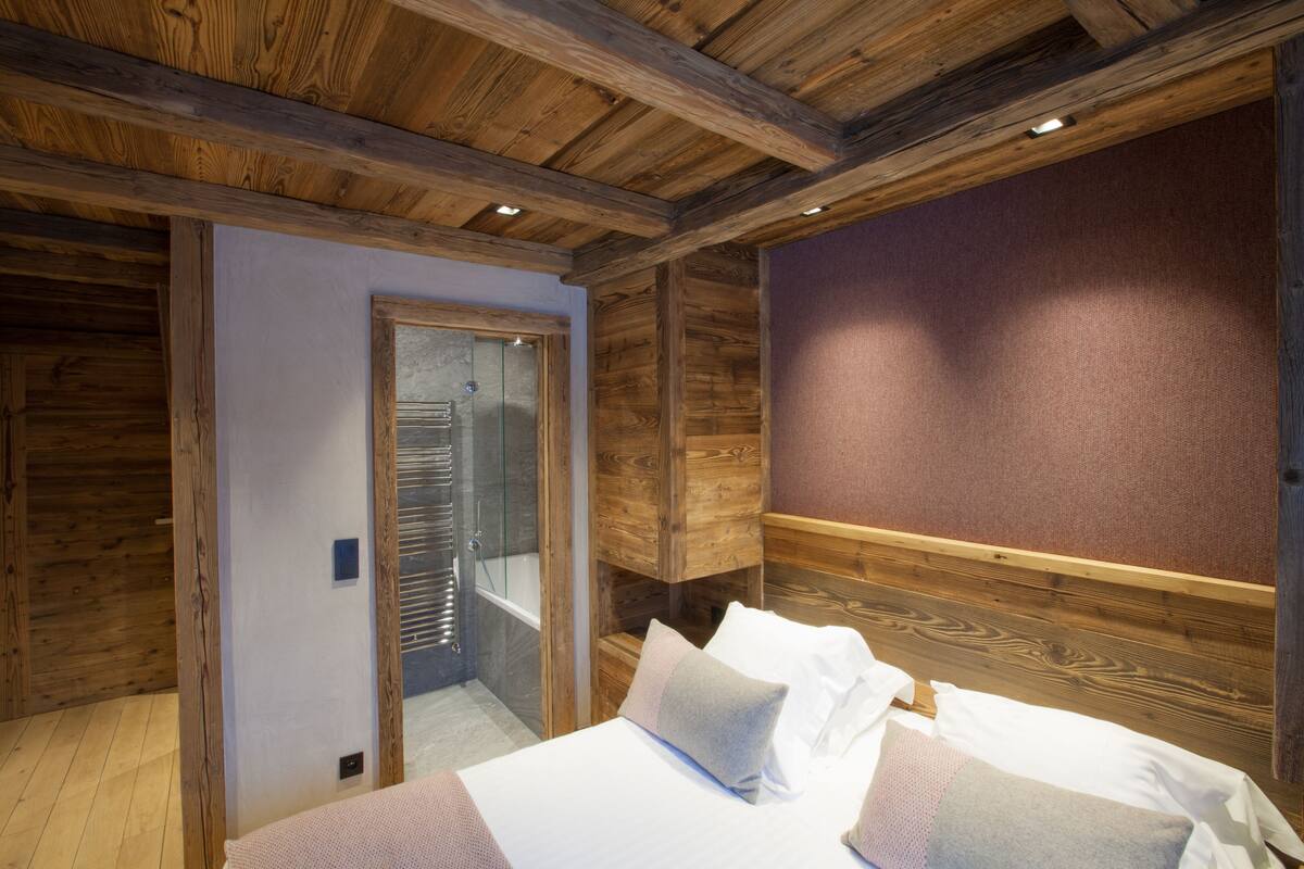Ein Zimmer mit Holzwänden, einem Bett, einer Dusche und einer Tür zu einem Badezimmer.