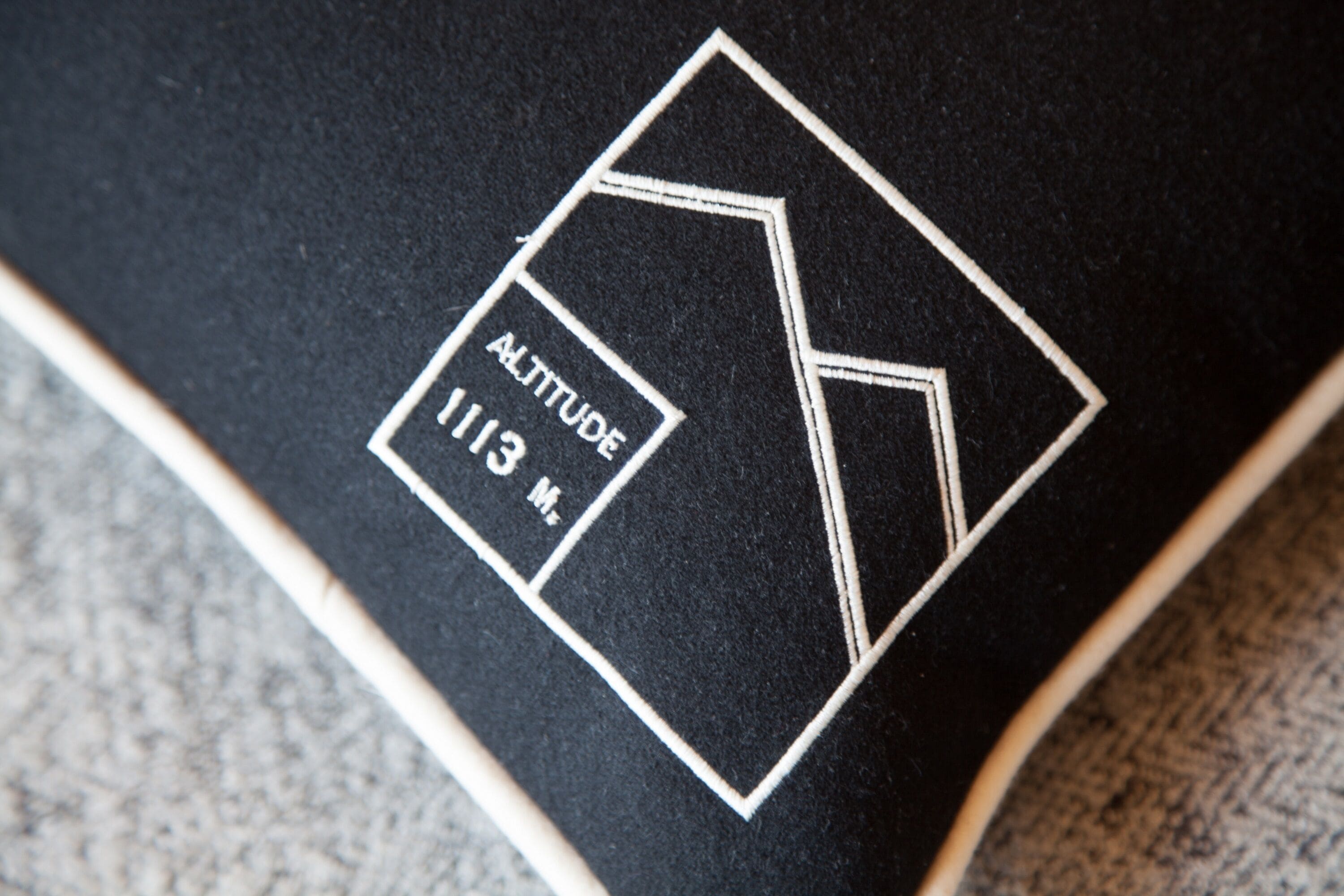 A black surface with a white geometric logo and the text "ALTITUDE 113 M."