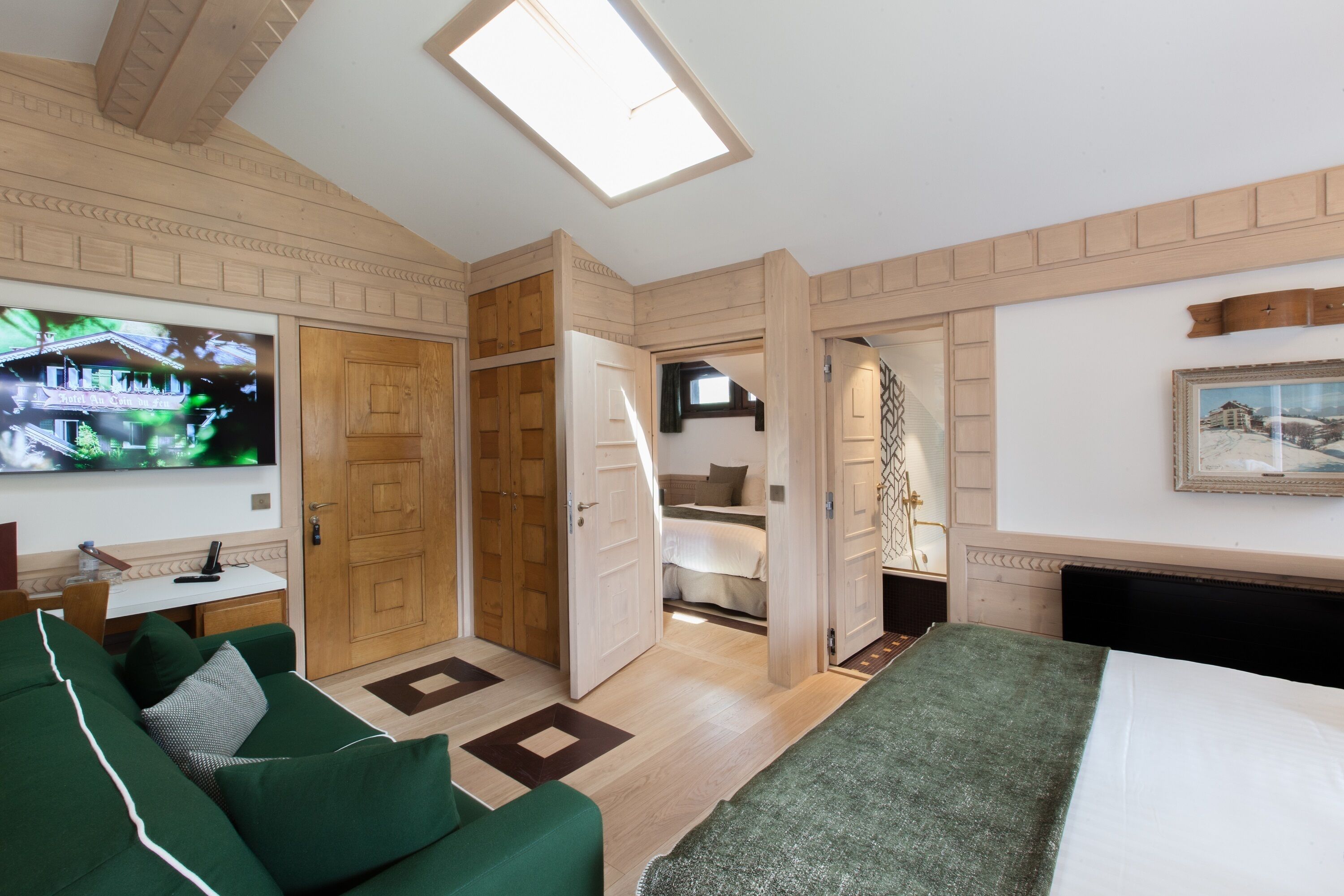A hotel room with a bed, a green sofa, a TV, a wooden wardrobe, and a painting on the wall.