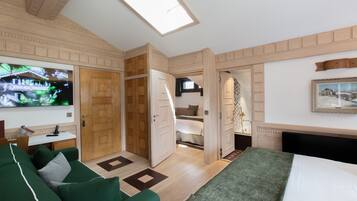 A hotel room with a bed, a green sofa, a TV, a wooden wardrobe, and a painting on the wall.