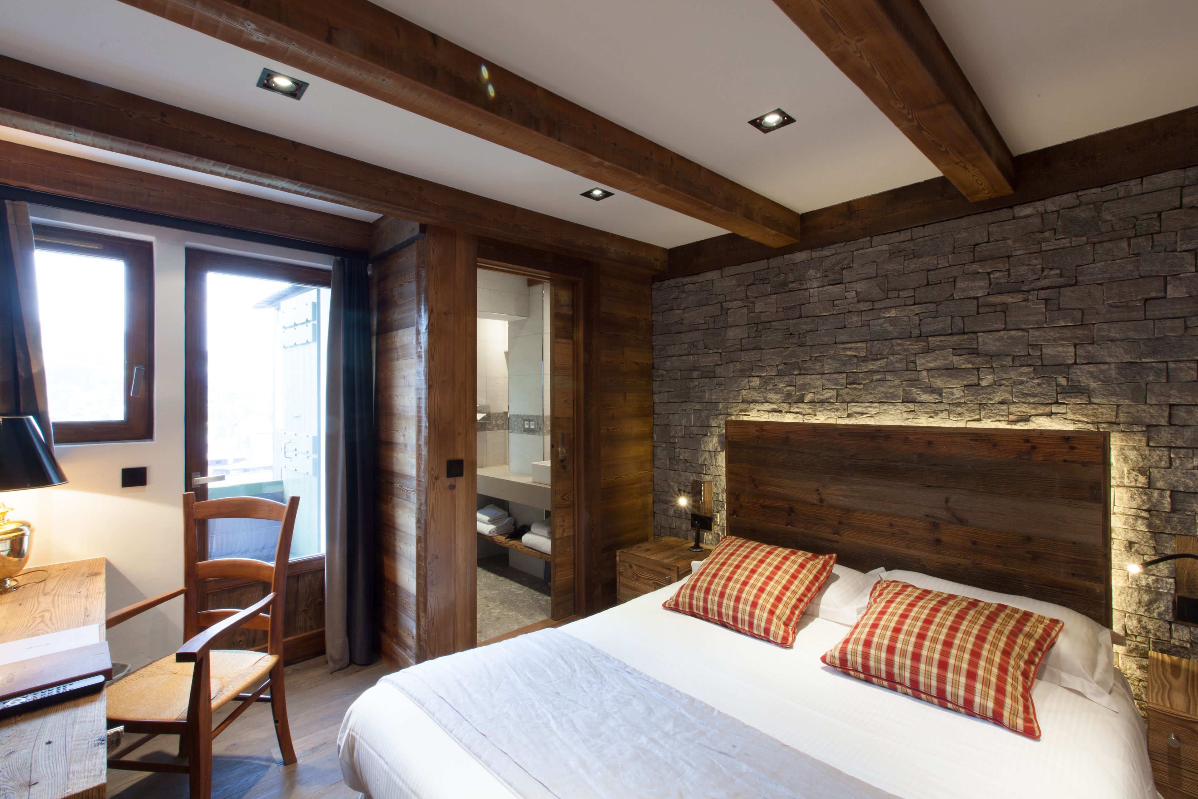 A bedroom with a stone wall, wooden headboard, and a bed with two pillows.