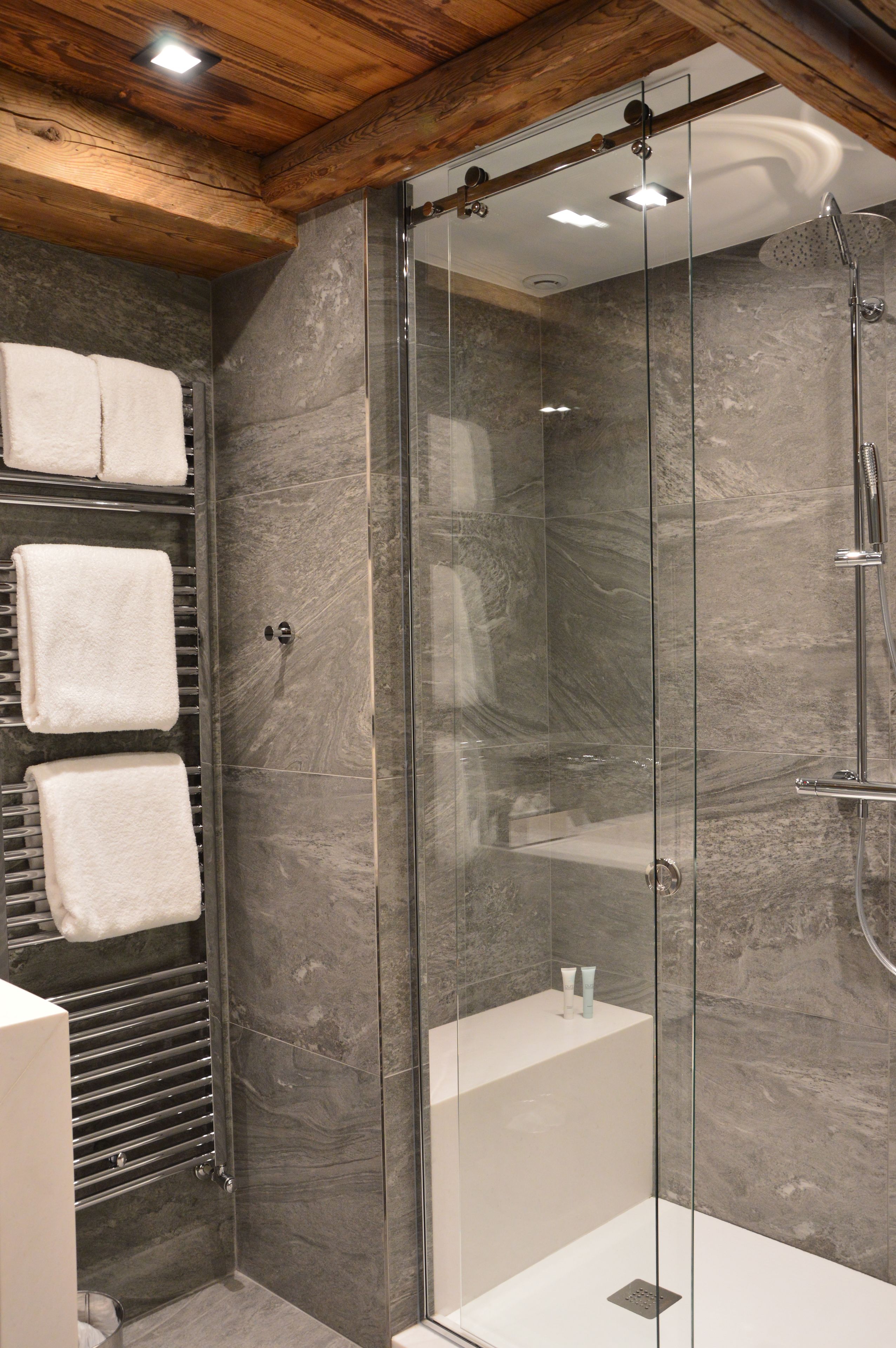 A modern bathroom with a glass-enclosed shower, a towel rack with multiple towels, and a marble wall.