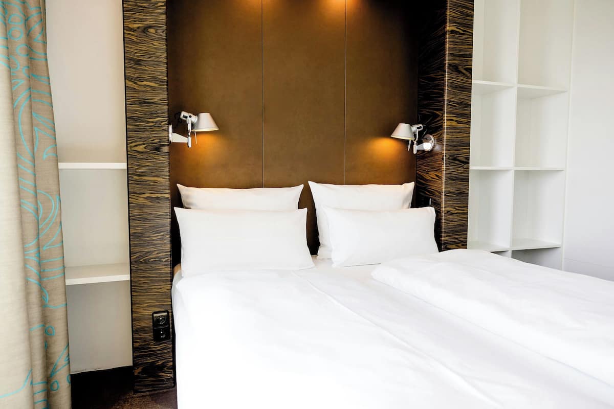 A hotel room with a large bed, two bedside lamps, and a wooden accent wall.