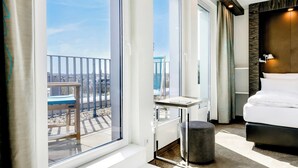 Una habitación de hotel con un ventanal grande, una cama, una mesita y una silla.
