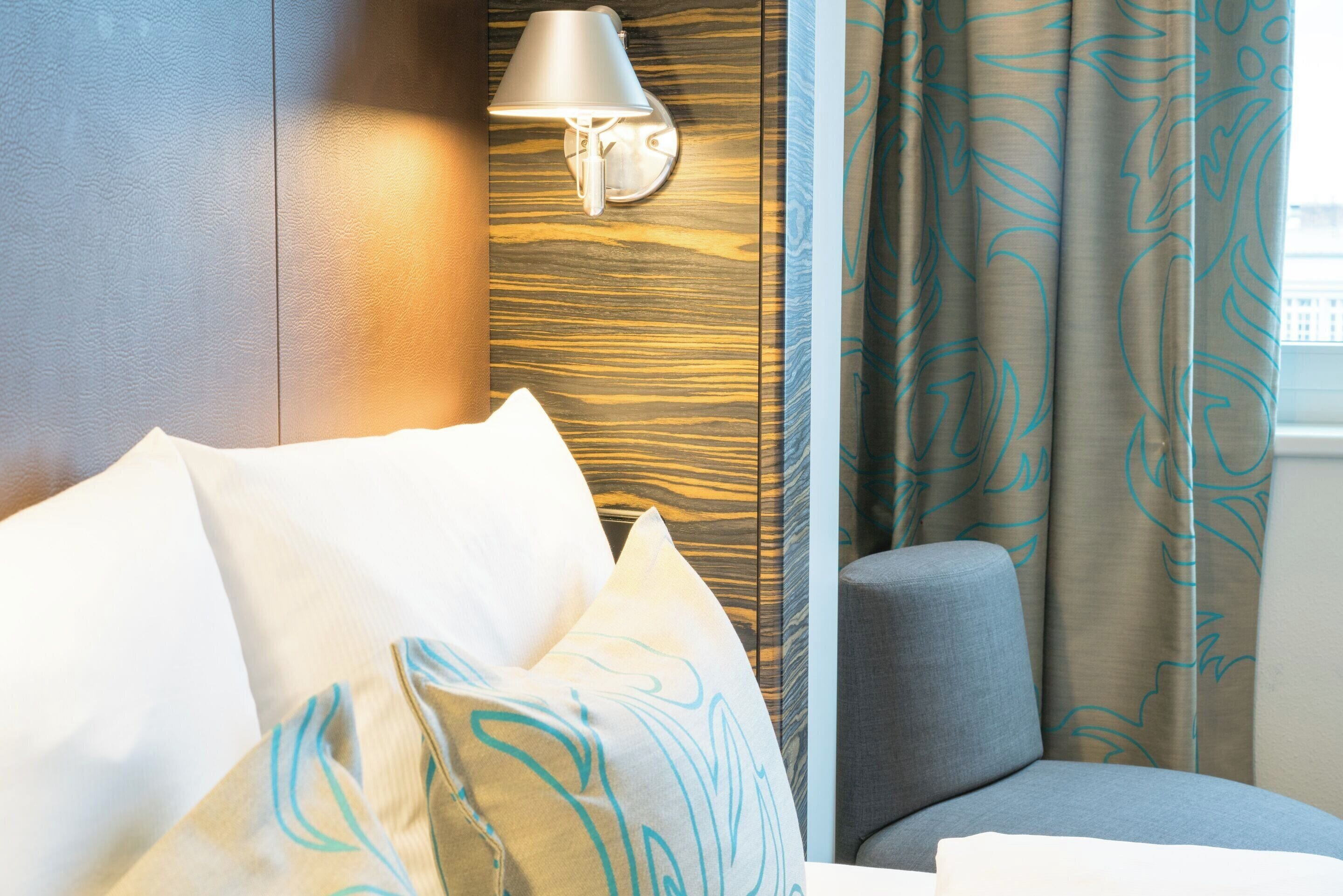 A hotel room with a bed, a nightstand, a lamp, and a window with curtains.