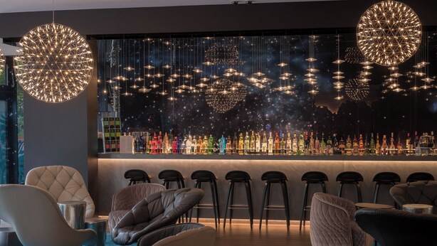 Un área de bar moderna con una fila de taburetes, una variedad de botellas de licor y luces decorativas colgantes.