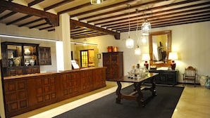 A reception area with a wooden reception desk, a large mirror, and a table with a vase and candle. - Parador de Santillana Altamira (Santillana del Mar)