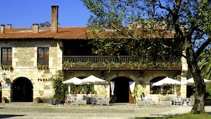 A historic building with a courtyard, outdoor seating, and flower beds. - Parador de Santillana Altamira (Santillana del Mar)