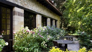 A stone building with large windows and a garden with various plants and flowers. - Parador de Santillana Altamira (Santillana del Mar)