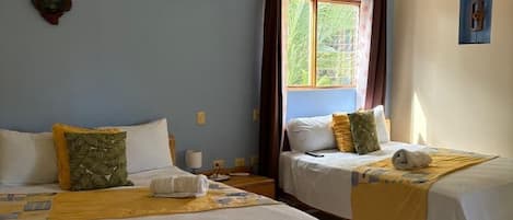 A hotel room with two beds, a ceiling fan, an air conditioning unit, and a window with curtains.