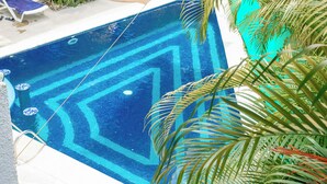 Una piscina con un motivo geometrico in piastrelle, circondata da poltroncine e palme.
