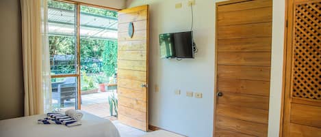 Habitación de hotel con dos camas, un ventilador de techo, un televisor montado en la pared y un ventanal corredero que da a un área exterior.