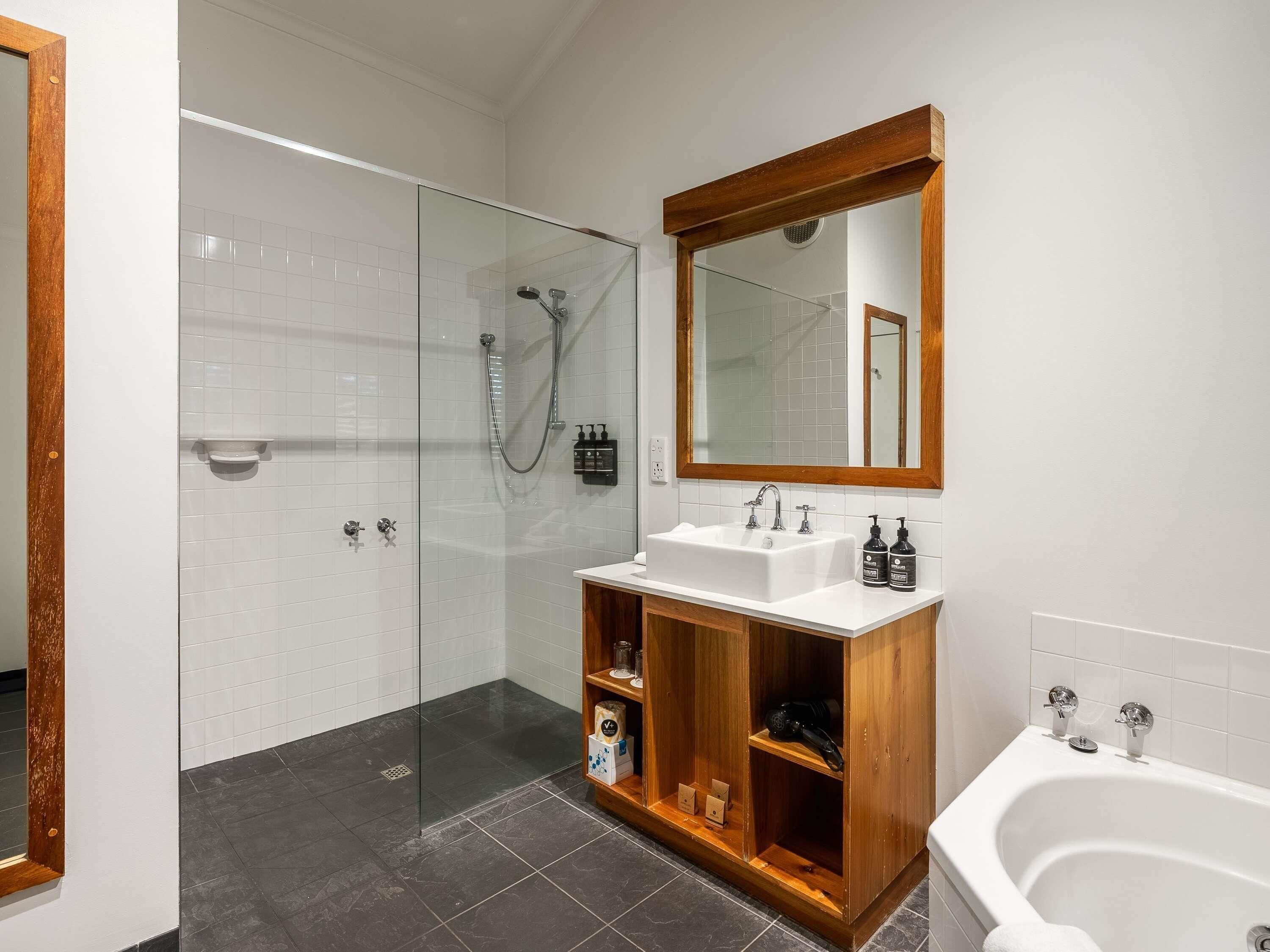 A modern bathroom with a glass-enclosed shower, a wooden vanity with a sink, and a large mirror.