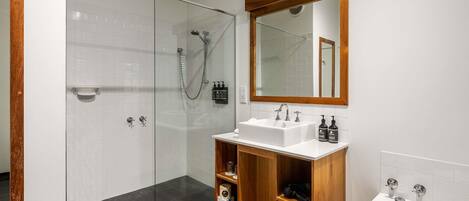A modern bathroom with a glass-enclosed shower, a wooden vanity with a sink, and a large mirror.