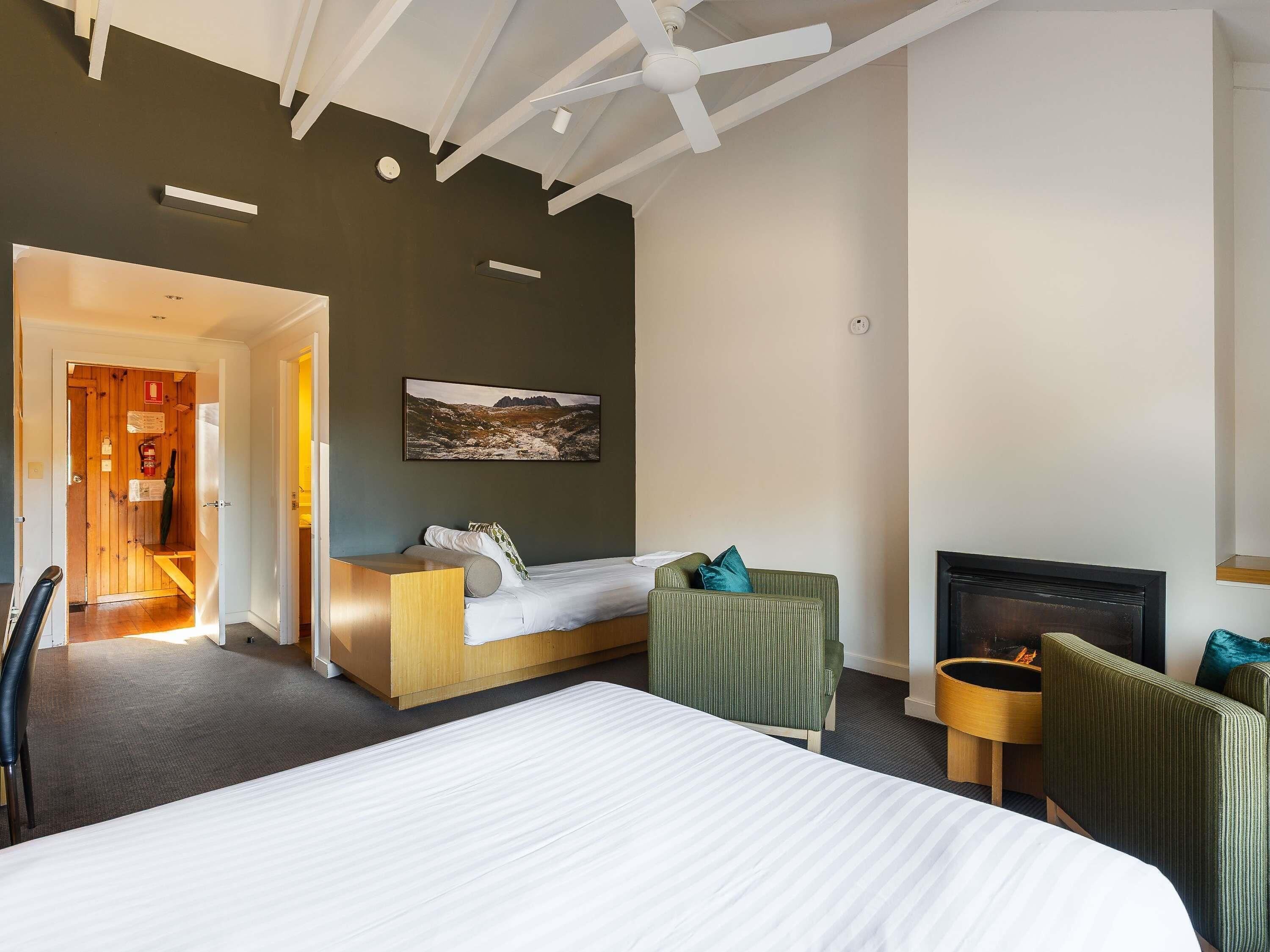 Una habitación de hotel con una cama, una zona de estar con sillas, una chimenea y un cuadro en la pared.