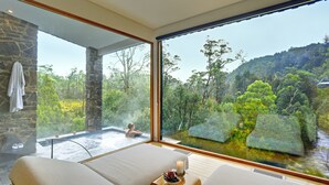 Un cuarto de spa con un amplio ventanal que da a una zona boscosa y una bañera de hidromasaje.