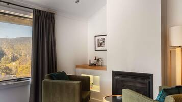 A hotel room with a bed, two armchairs, a small table, a fireplace, a window with curtains, and a picture on the wall.