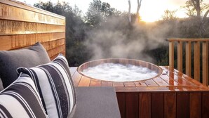 Un jacuzzi con vapor, rodeado de una terraza de madera y mobiliario exterior.