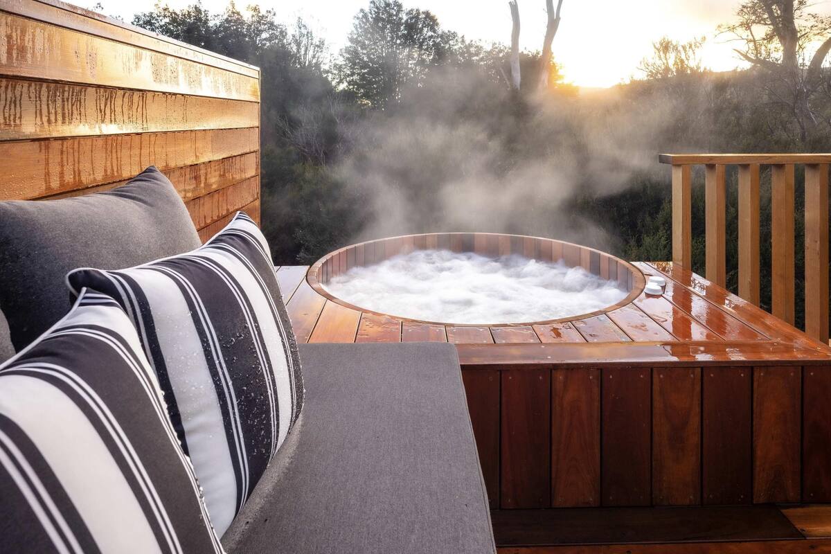Een hottub met stoom, omringd door een houten terras en tuinmeubilair.