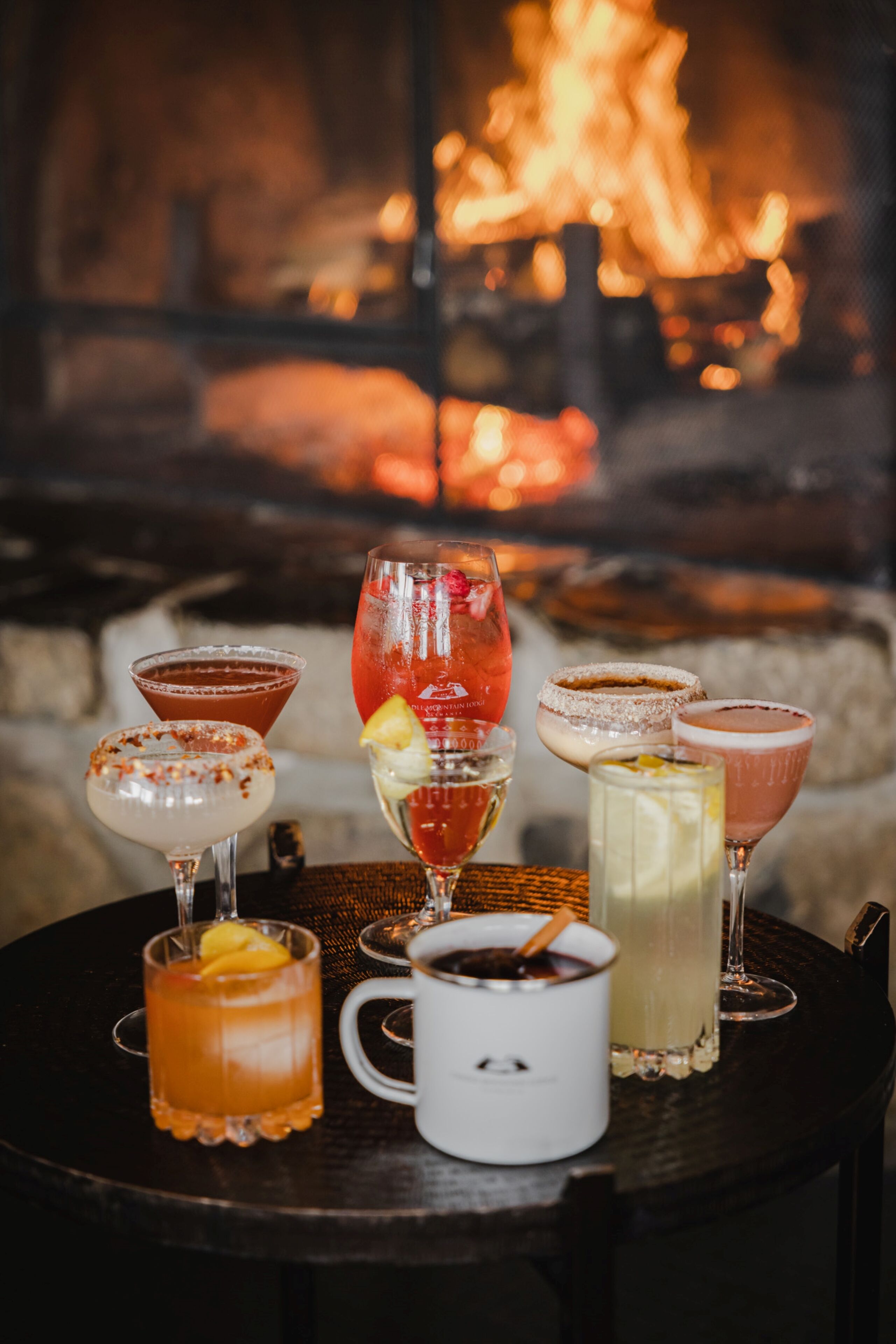 A table with various drinks and a white mug, set against a fireplace backdrop.