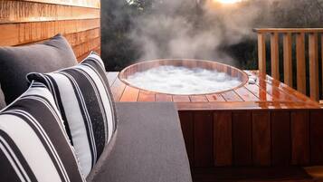 A hot tub with steam rising, surrounded by wooden deck and a sofa with striped cushions.