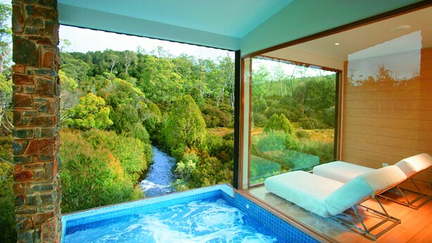 Un cuarto de spa con hidromasaje, vistas a una zona boscosa y una pared de ladrillo.