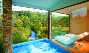 Een wellnessruimte met een jacuzzi, uitzicht op een bebost gebied en een bakstenen muur.