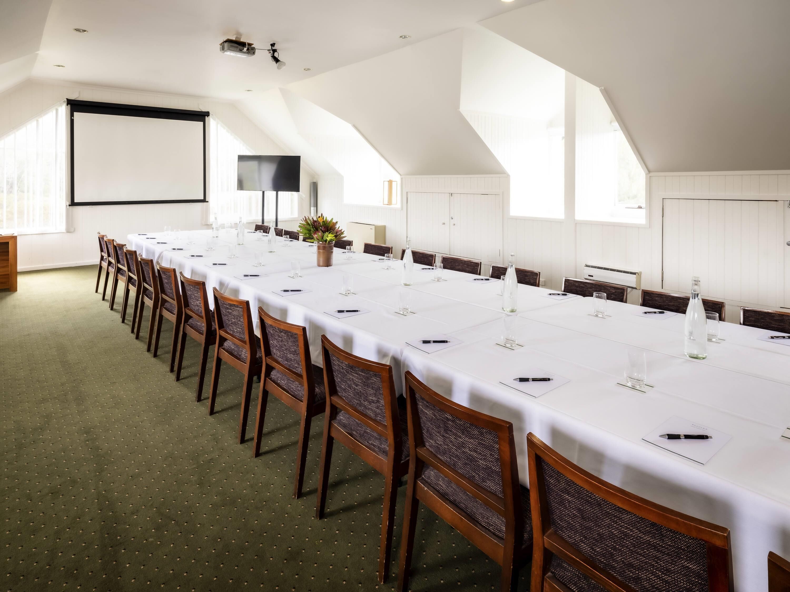 Une salle de conférence avec une longue table, des chaises, un écran de projection et une grande fenêtre.