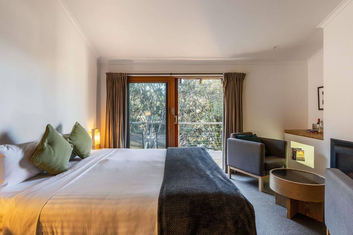 Hotelkamer met een bed, zithoek, een klein tafeltje en een balkon met uitzicht op bomen.