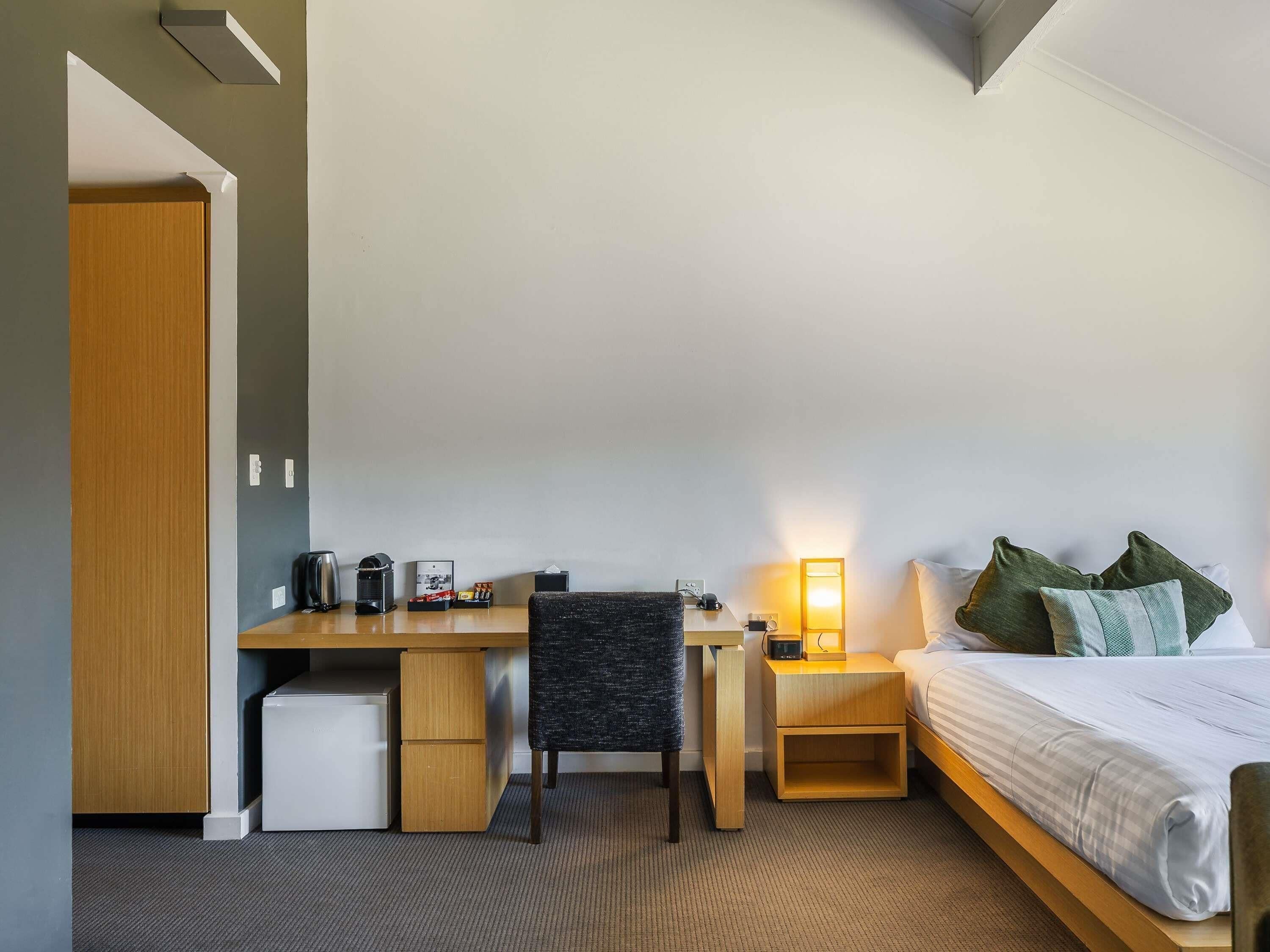 Habitación de hotel con cama, escritorio, silla y un refrigerador pequeño.