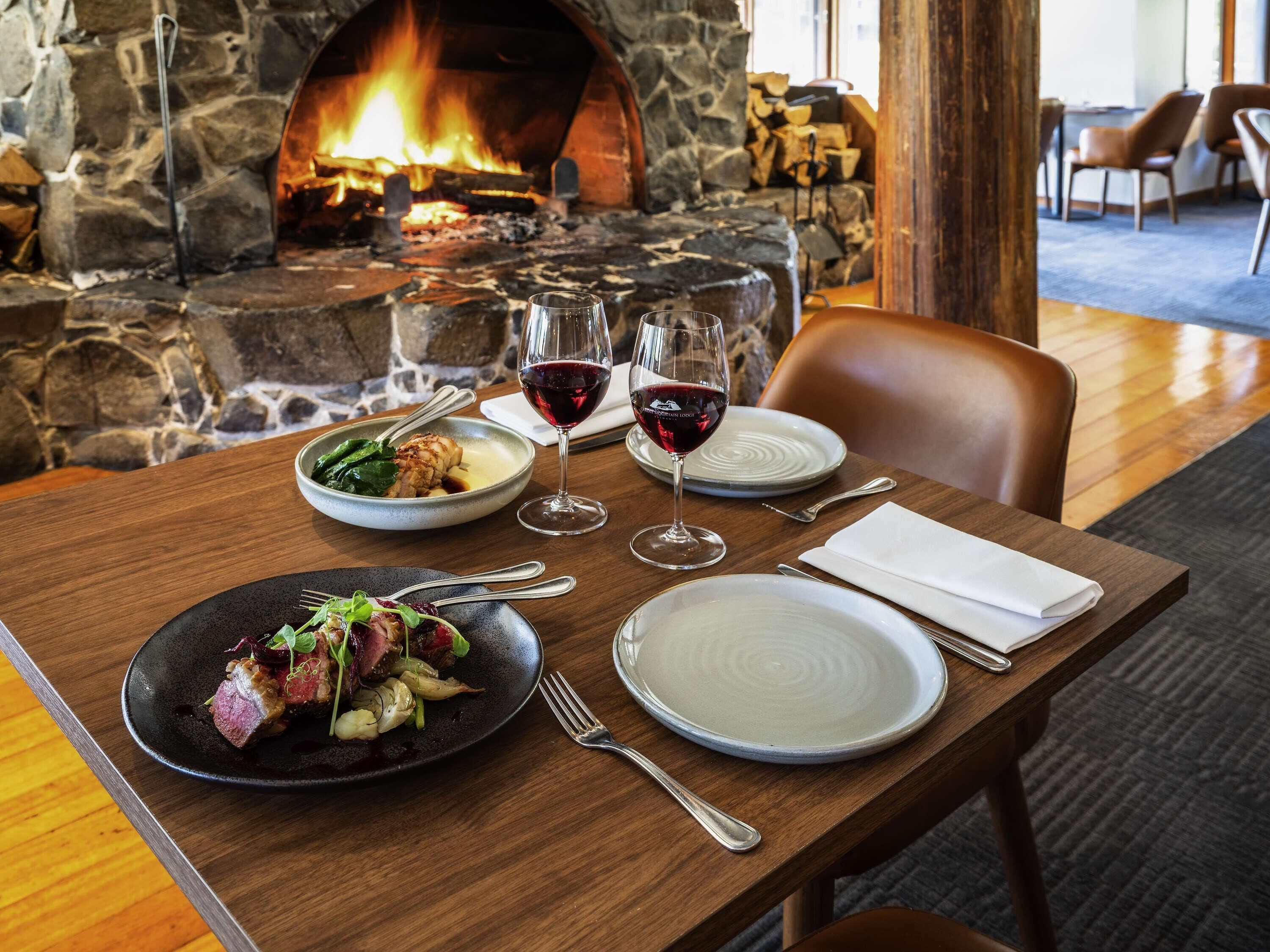 Une table à manger dressée avec des assiettes, des couverts et des verres, avec une cheminée en pierre en arrière-plan.
