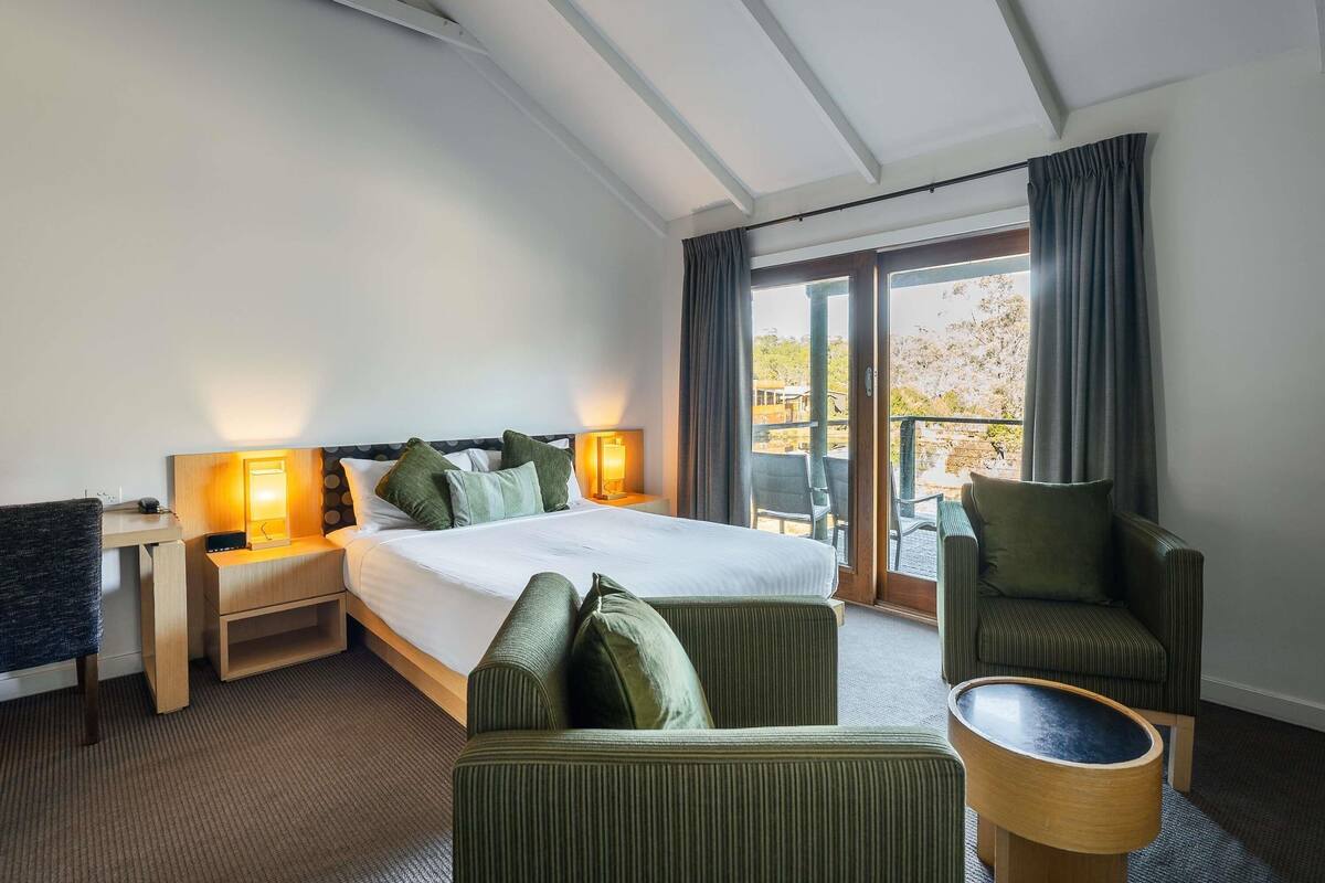 Een hotelkamer met een bed, twee nachtkastjes met lampen, een bank, een fauteuil en uitzicht op het landschap.