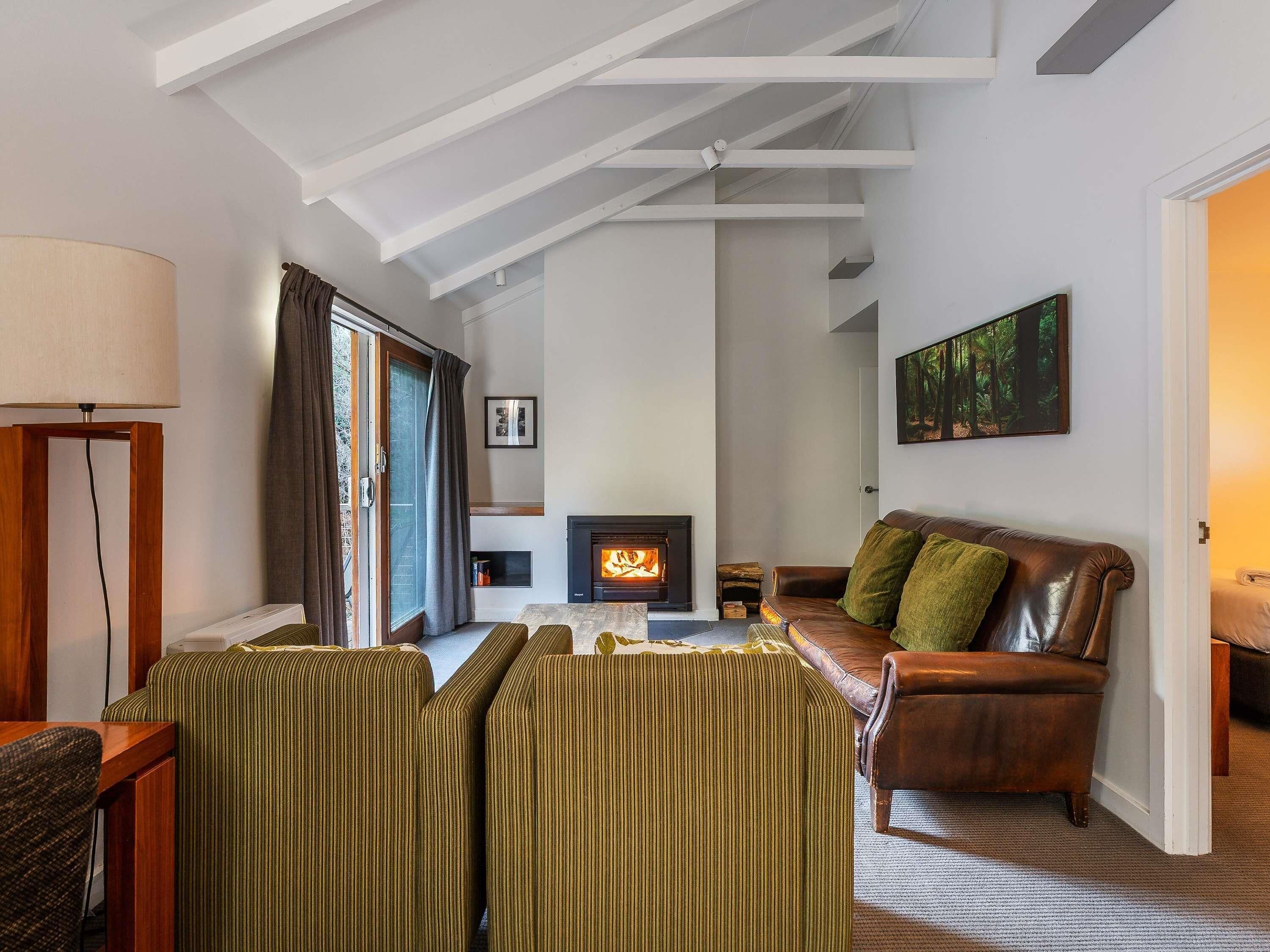 Una sala de estar con chimenea, un sofá, un sillón a rayas, una lámpara y un cuadro en la pared.