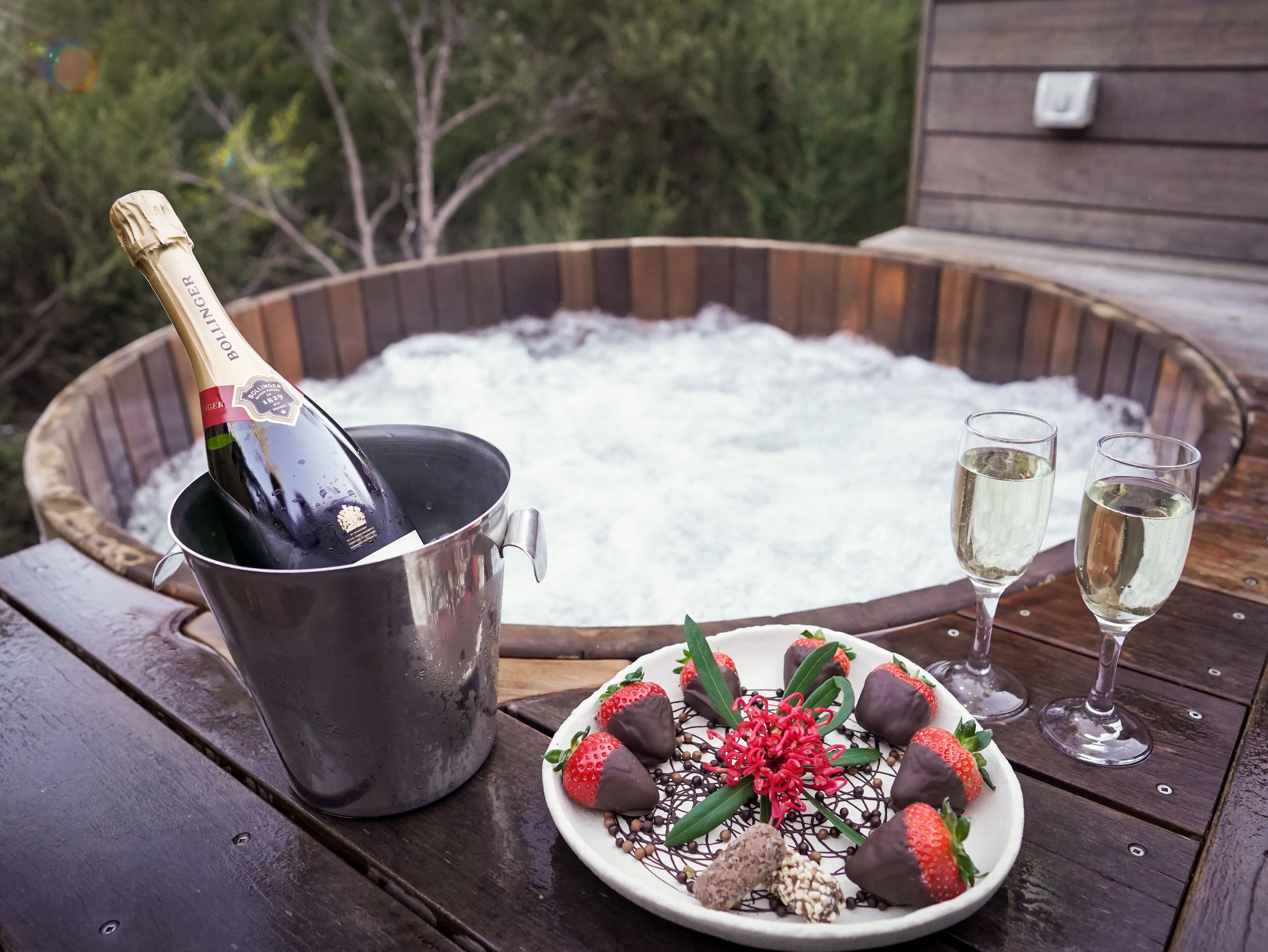 Un bain à remous avec une bouteille de champagne et deux coupes de champagne sur une terrasse en bois.
