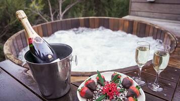 A hot tub with a bottle of champagne and two glasses of champagne on a wooden deck.