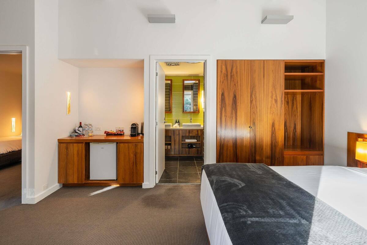 Hotelkamer met een bed, bureau, kleine koelkast, houten garderobe en een badkamer door een geopende deur zichtbaar.