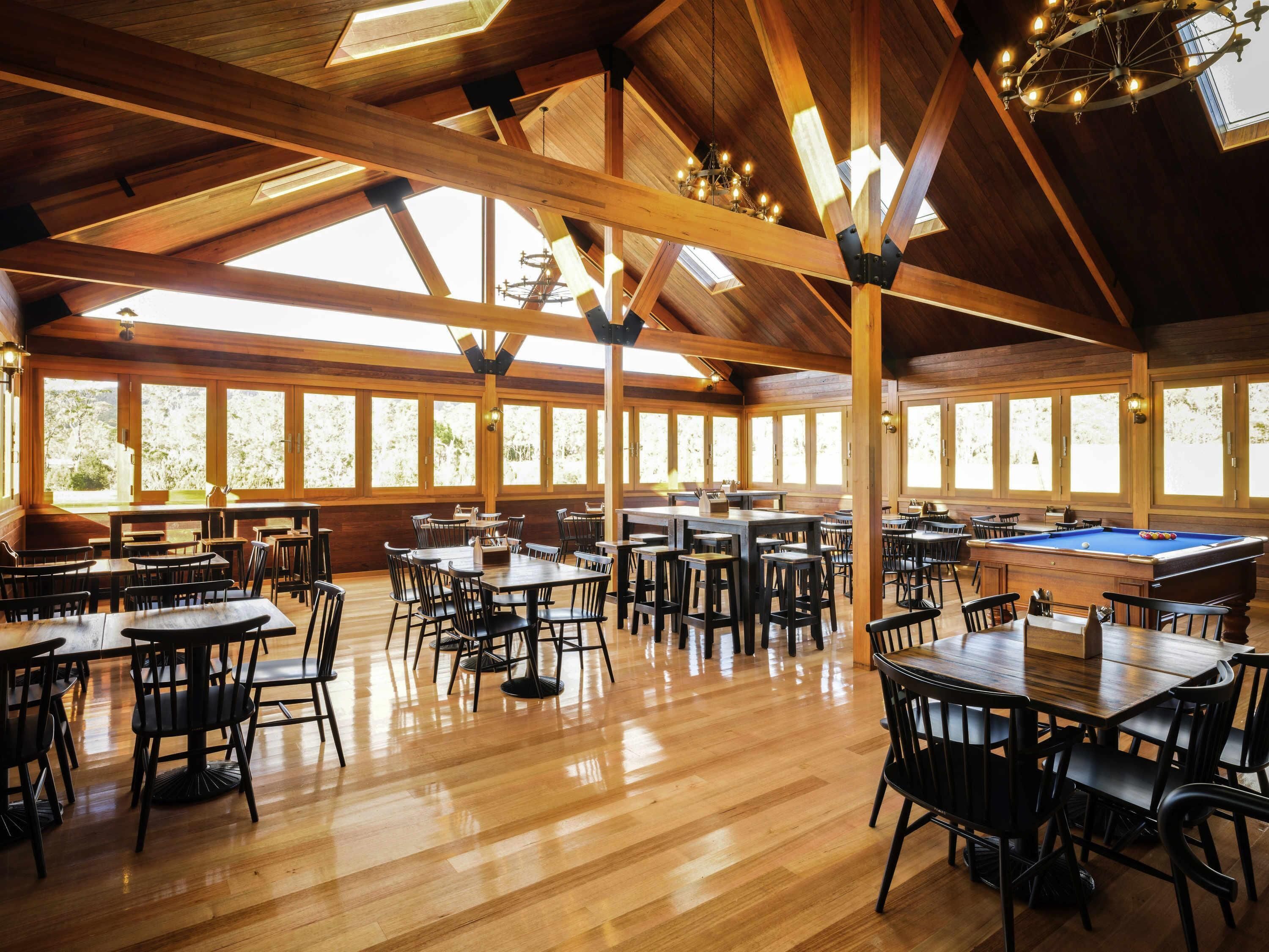 Un grand espace intérieur doté de poutres en bois, de tables, de chaises et d’un billard.