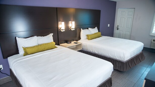 A hotel room with two beds, a nightstand, and a door. - Atlantic Inn (Indialantic)