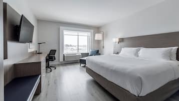 Une chambre d’hôtel avec un grand lit, un bureau, une chaise, une télévision et une fenêtre donnant sur l’extérieur.