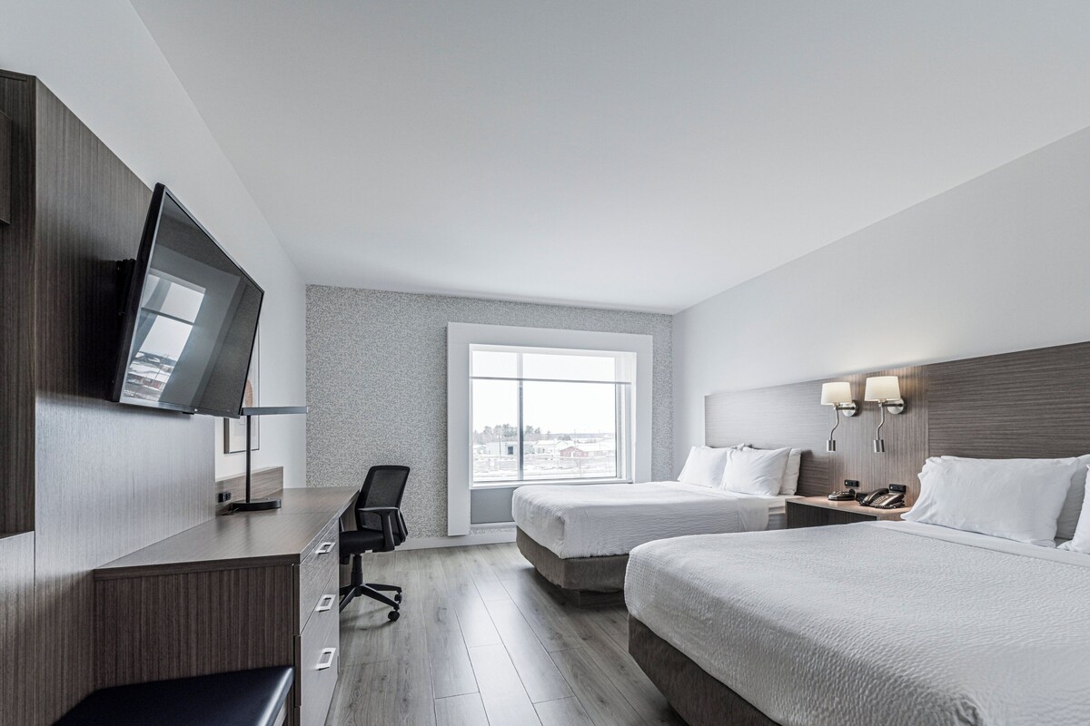 Ein Hotelzimmer mit zwei Betten, einem Schreibtisch, einem Sessel, einem Fernseher und einem Fenster mit Blick.