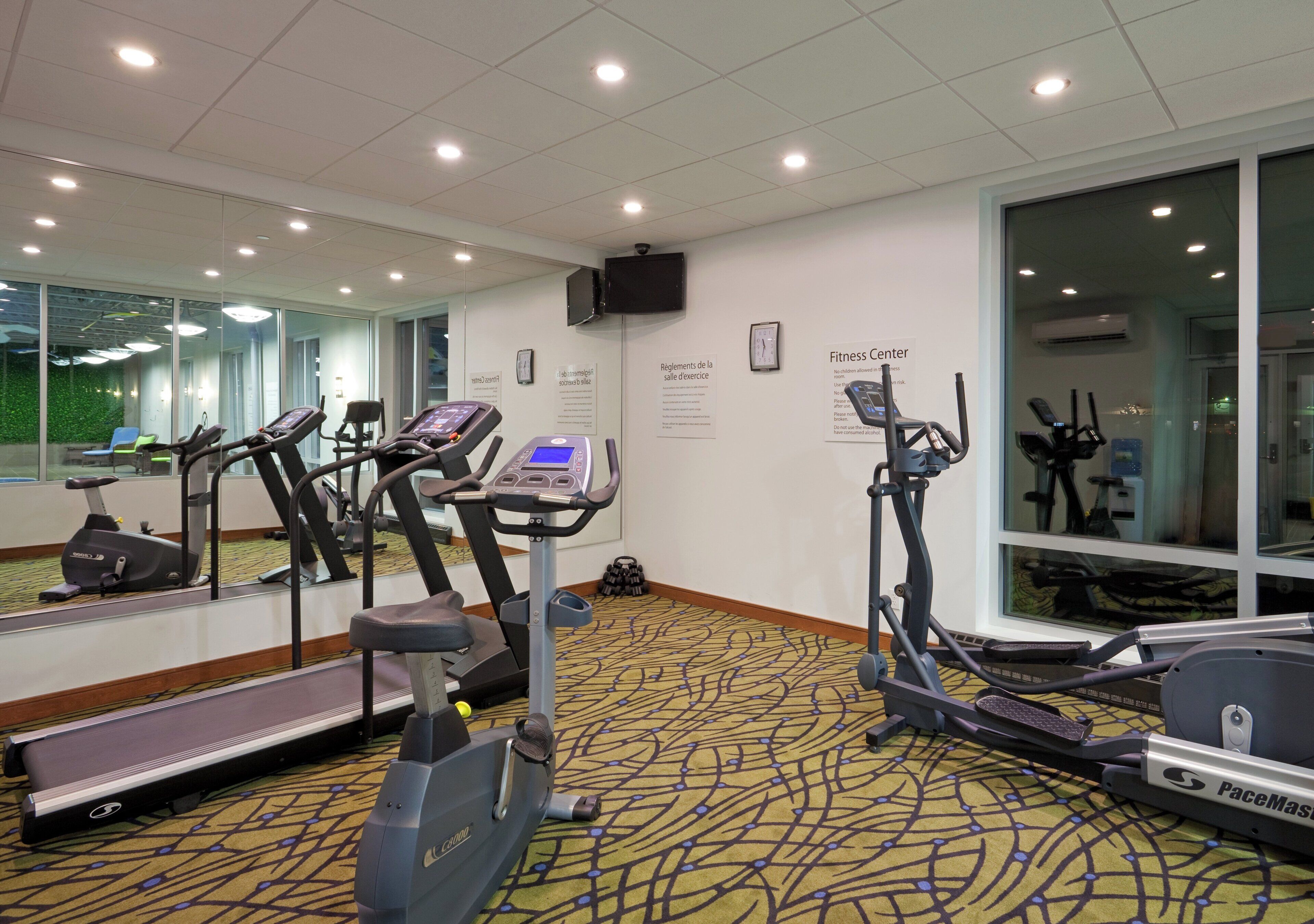 A fitness center with treadmills, elliptical machines, and a mirrored wall.